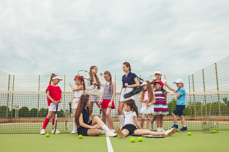 portrait group girls boy as tennis players holding tennis rackets against green grass outdoor court